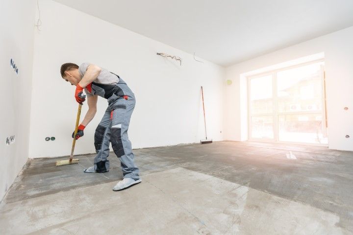 A man is cleaning the floor with a broom in an empty room.
