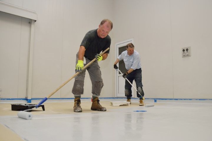 Two men are painting a white floor with rollers.