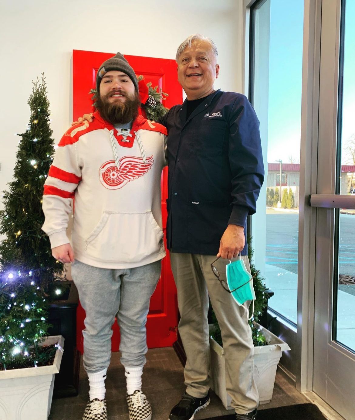 two men are posing for a picture in front of a red door .