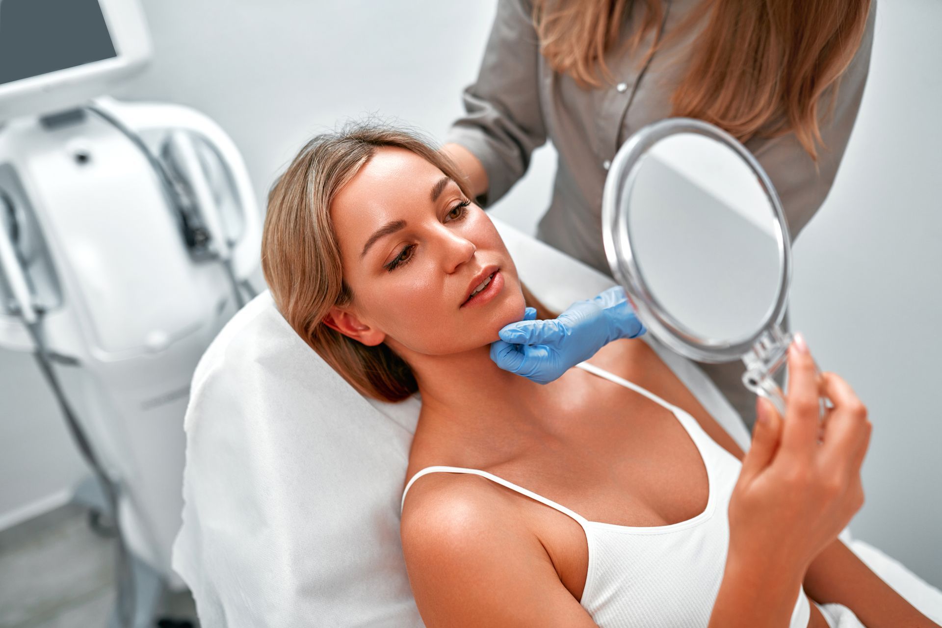 A woman is looking at her face in a mirror.