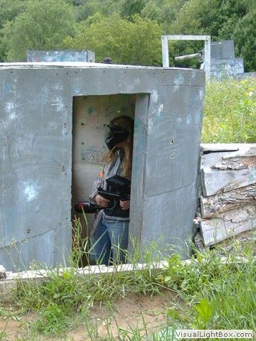 Person peering through a small doorway in a concrete structure, outdoors in overgrown grass.