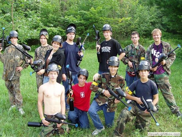 Group of people in paintball gear posing with markers in a wooded outdoor setting