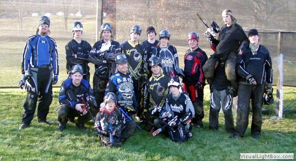 Group of paintball players posing outdoors in blue and black gear, some holding markers
