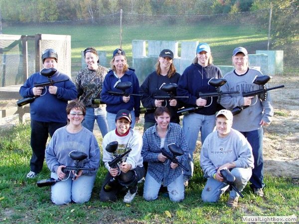Group of people in tactical gear posing outdoors on a grassy field holding paintball markers