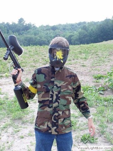 Person in camouflage holding a paintball gun outdoors on a grassy field.