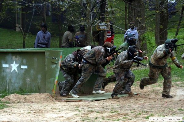 Camouflaged players crouch and sprint during an outdoor paintball game in a wooded field.