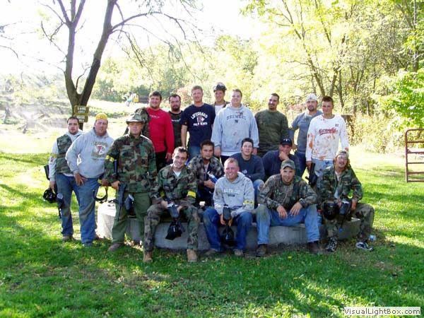 Group of people posing outdoors in a grassy park with trees and bright sunlight