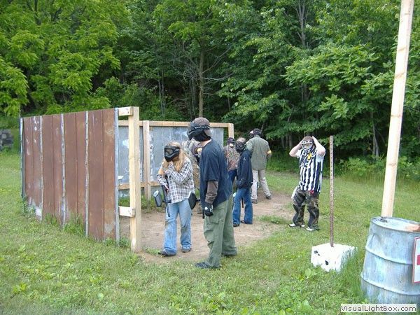 People standing by a wooden outdoor target range in a grassy clearing near trees