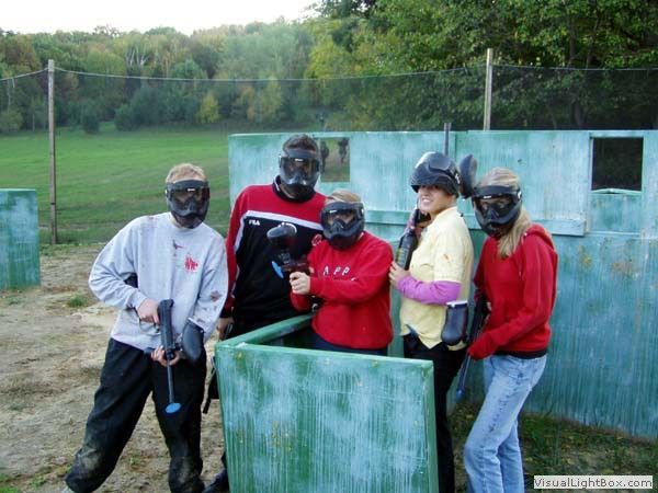 Five paintball players in masks standing behind bunker cover on a grassy field