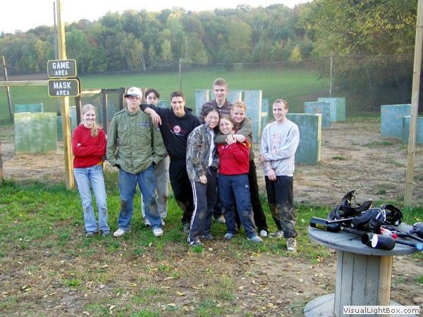 Group of people posing outdoors by a dirt range with a sign and shooting gear on a table