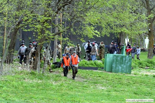 People in orange vests walking through a wooded paintball field with green barriers