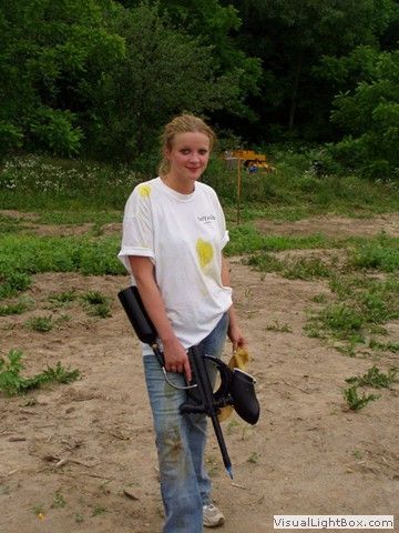 Person standing outdoors holding a rifle, wearing a white T-shirt and jeans.