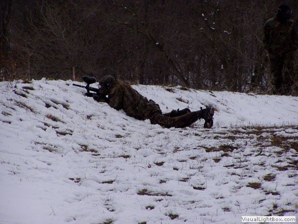 Person crawling through snow with a rifle in a wooded area