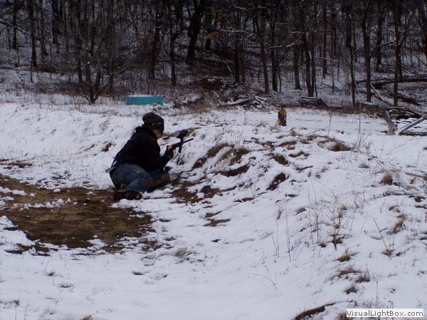 Person kneeling in snow aiming a camera in a wooded area