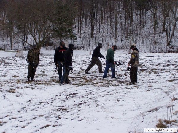 People standing and moving in a snowy forest clearing, with trees in the background.