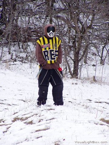 Person standing in snowy woods wearing a yellow-and-black striped jersey and black pants