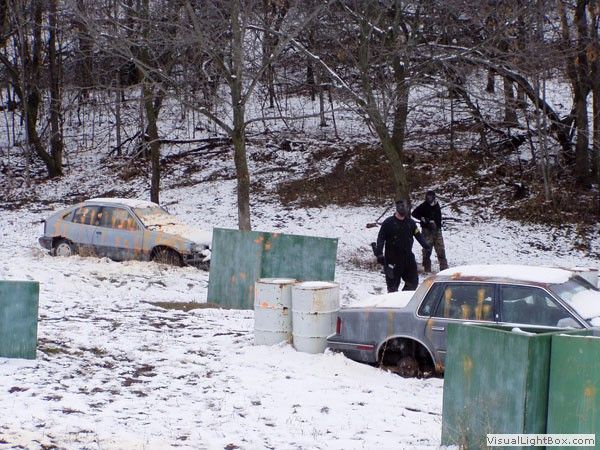 Snowy wooded roadside with two abandoned cars and two people standing beside a car in the foreground