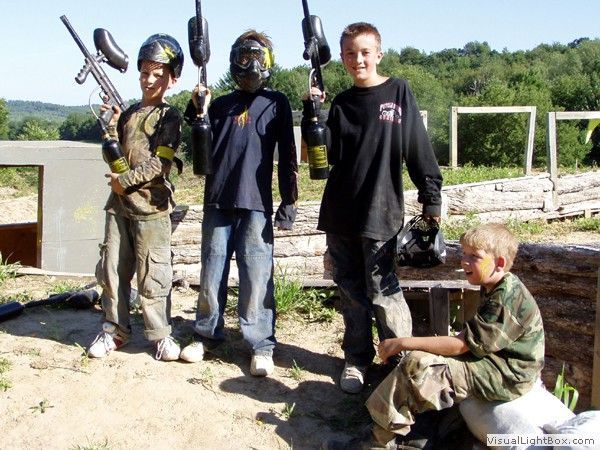 Four people posing outdoors in military-style gear, with one person crouching in the foreground.