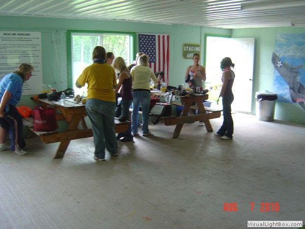 People gathered around picnic tables in a green hall with an American flag and a mural on the wall