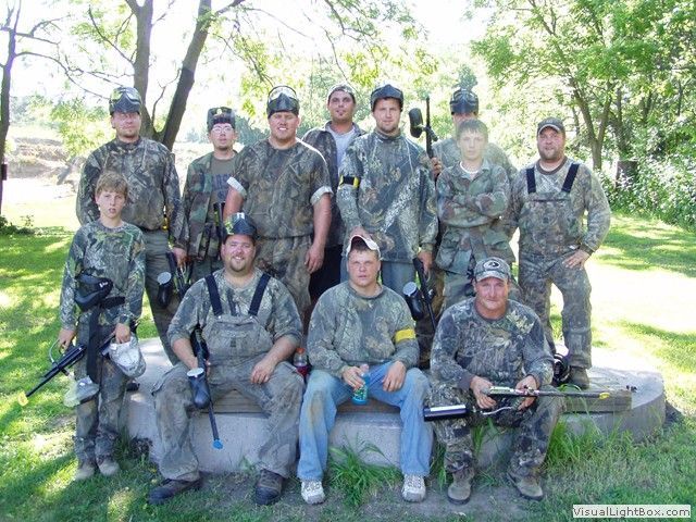Group of camouflage-clad hikers posing outdoors with rifles in a wooded area.
