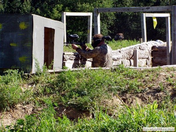 Two paintball players in helmets aiming markers behind white barriers on a grassy field