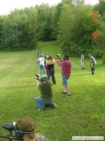 People target shooting at an outdoor range on a grassy field, with trees in the background.