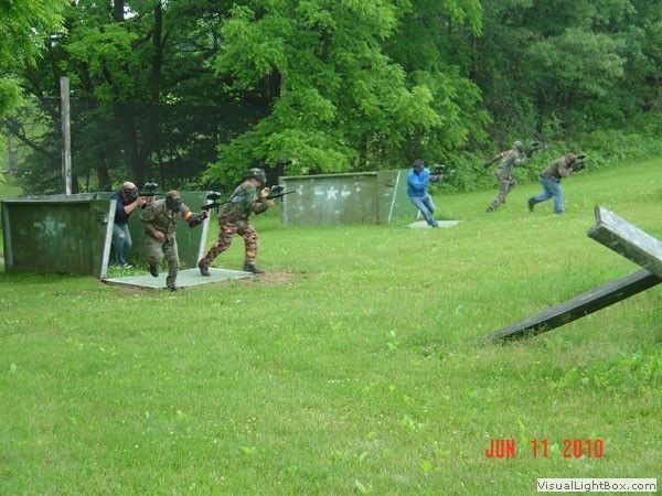 People in camouflage gear running and crouching behind barriers in a grassy outdoor field