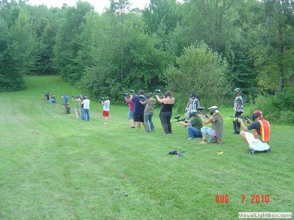 People practicing on a grassy field near trees, with several standing and kneeling in a line.