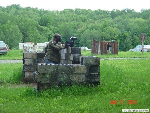 Person aiming a rifle from behind a concrete barrier on a grassy outdoor range.