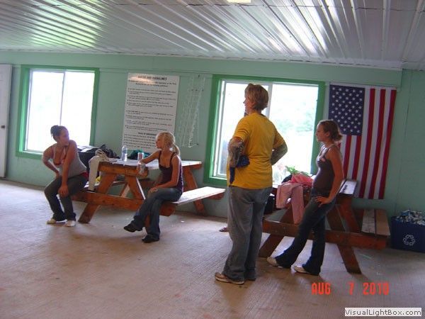 People sitting and standing in a room with a large American flag on the wall.