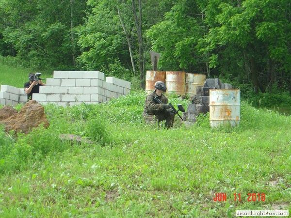 Soldiers taking cover behind concrete barriers in a grassy field with trees and barrels nearby