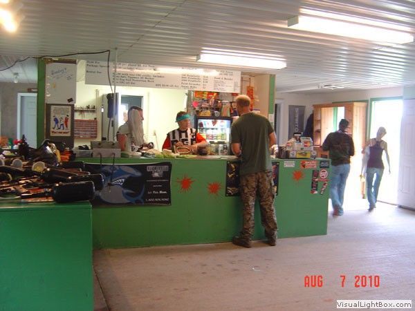 Indoor café with a green counter, people standing at the register, and a seated patron near the windows
