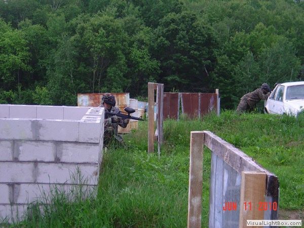 Rural paintball field with cinderblock barriers, a player behind cover, and a white SUV in the background