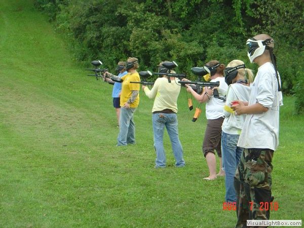 People aiming paintball guns at targets on a grassy outdoor field