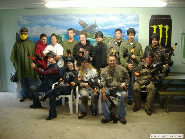 Group of people posing indoors in tactical and camouflage gear, with a Monster Energy banner on the wall.