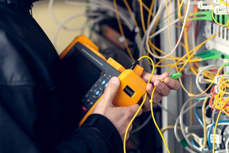 Person testing network cables with yellow testing equipment in a server room.