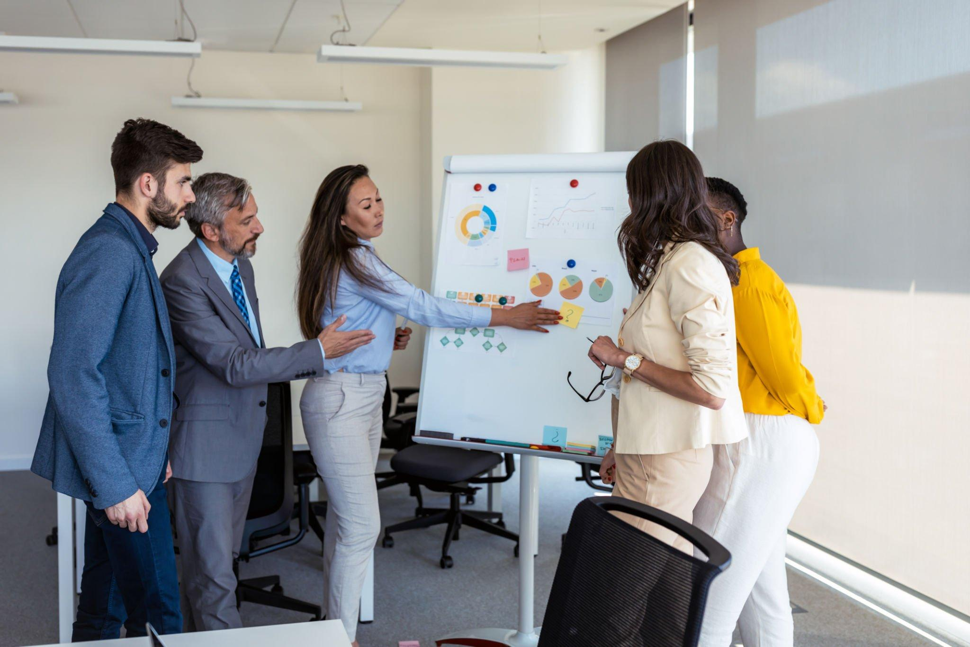 A group of people are standing around a whiteboard in an office.