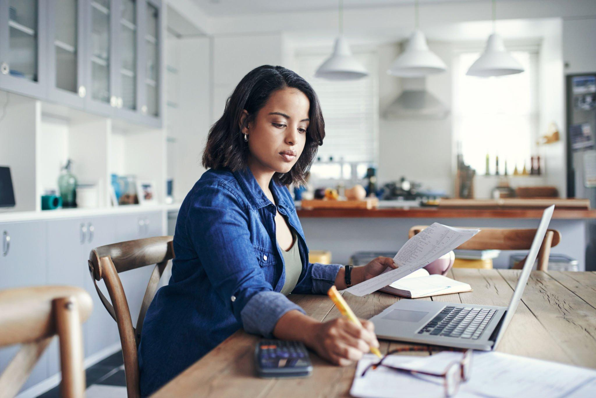 A woman is sitting at a table with a laptop and a calculator.