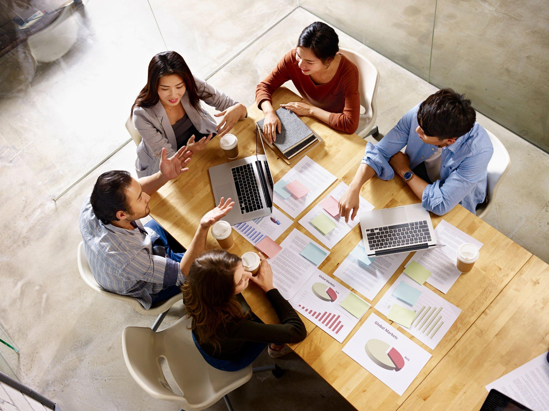 A group of people are sitting around a table with laptops and papers.