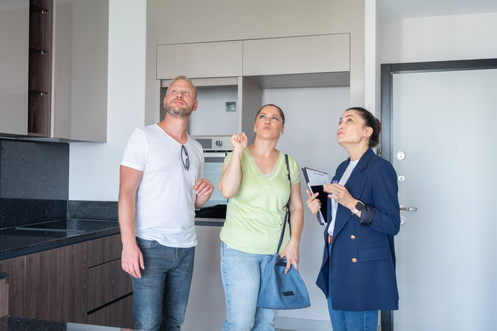 A man and two women are standing in a kitchen looking up at the ceiling.