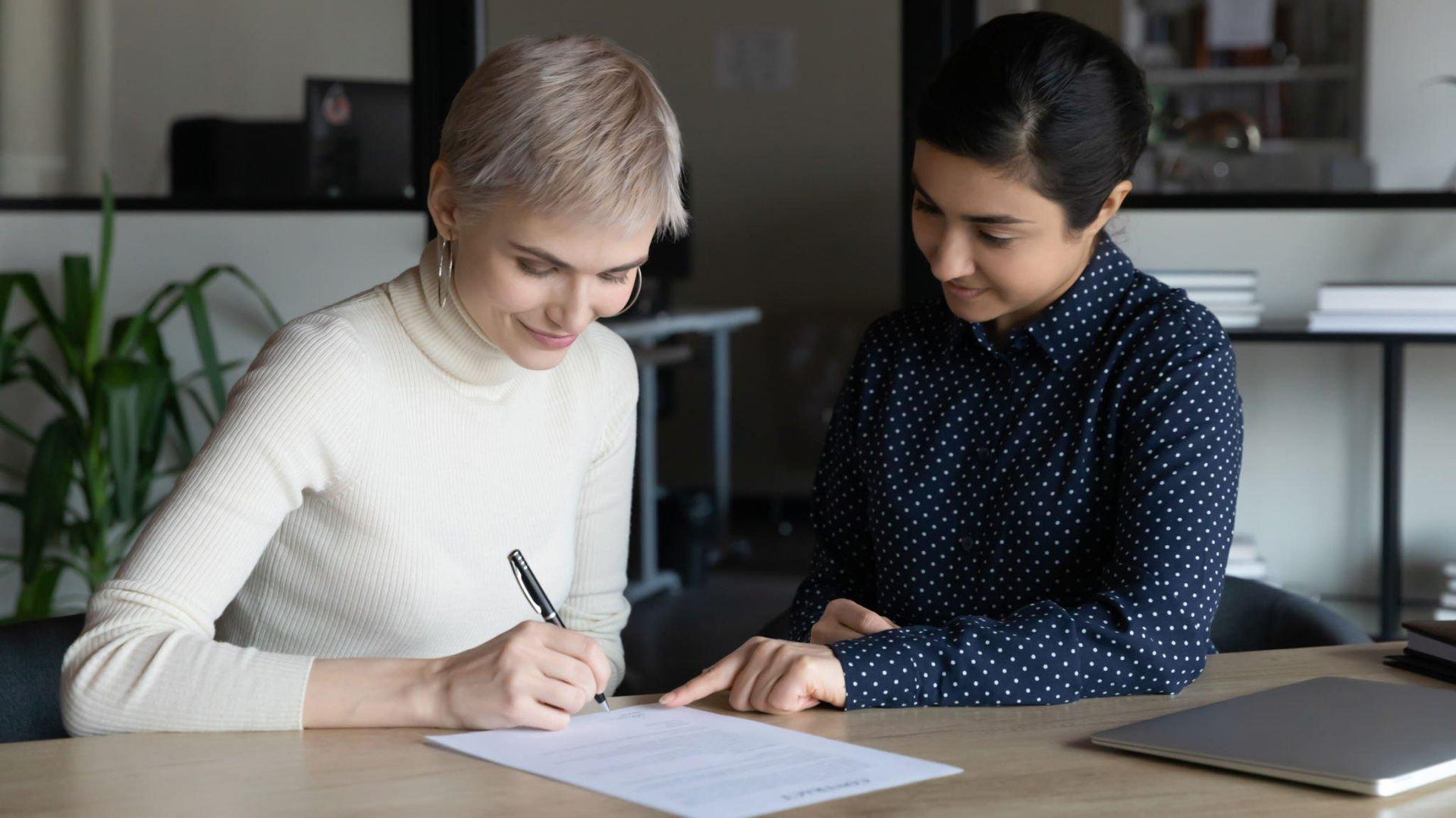 Two women are sitting at a table signing a document.