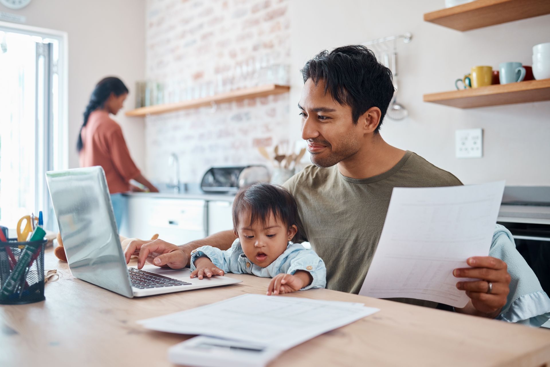 A man is holding a baby while using a laptop computer.