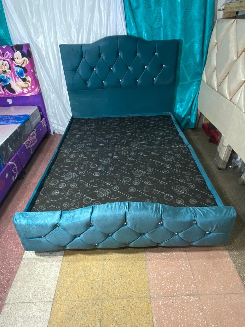 Estructura de cama tapizada en verde azulado con cabecero y pie de cama capitoné. Colchón con estampado negro.