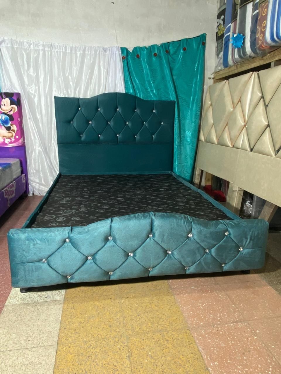 Cama tapizada en color verde azulado con cabecera y pie de cama capitoné, en interior.