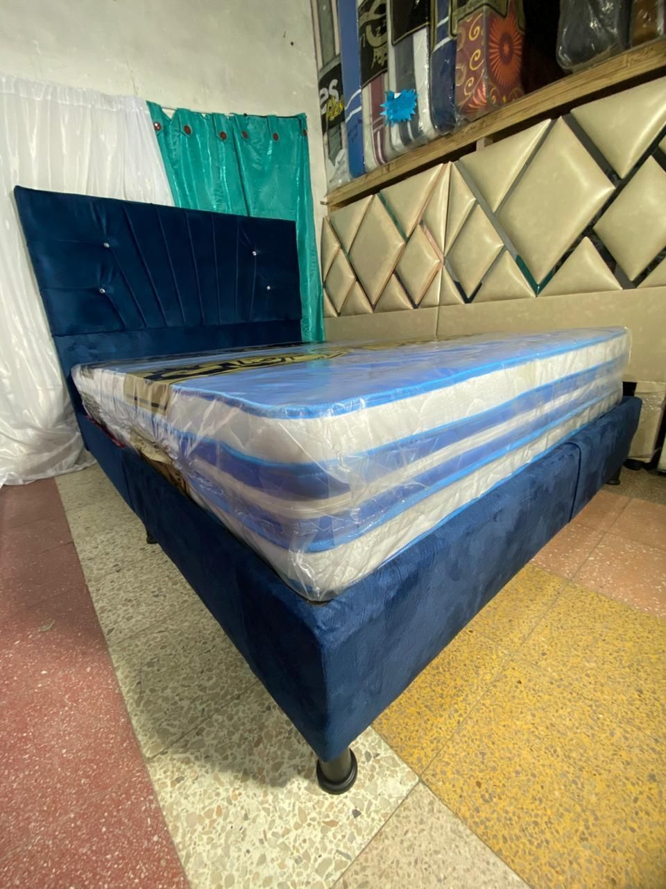 Cama tapizada en color azul con colchón, situada en un almacén.