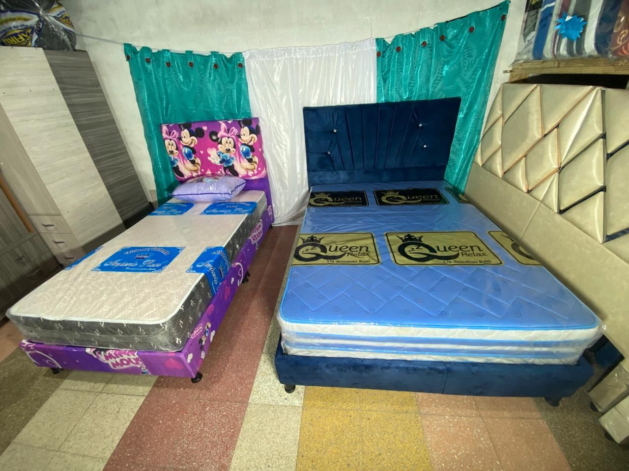 Dos camas con colchones y cabeceros en una habitación con cortinas y otros muebles.