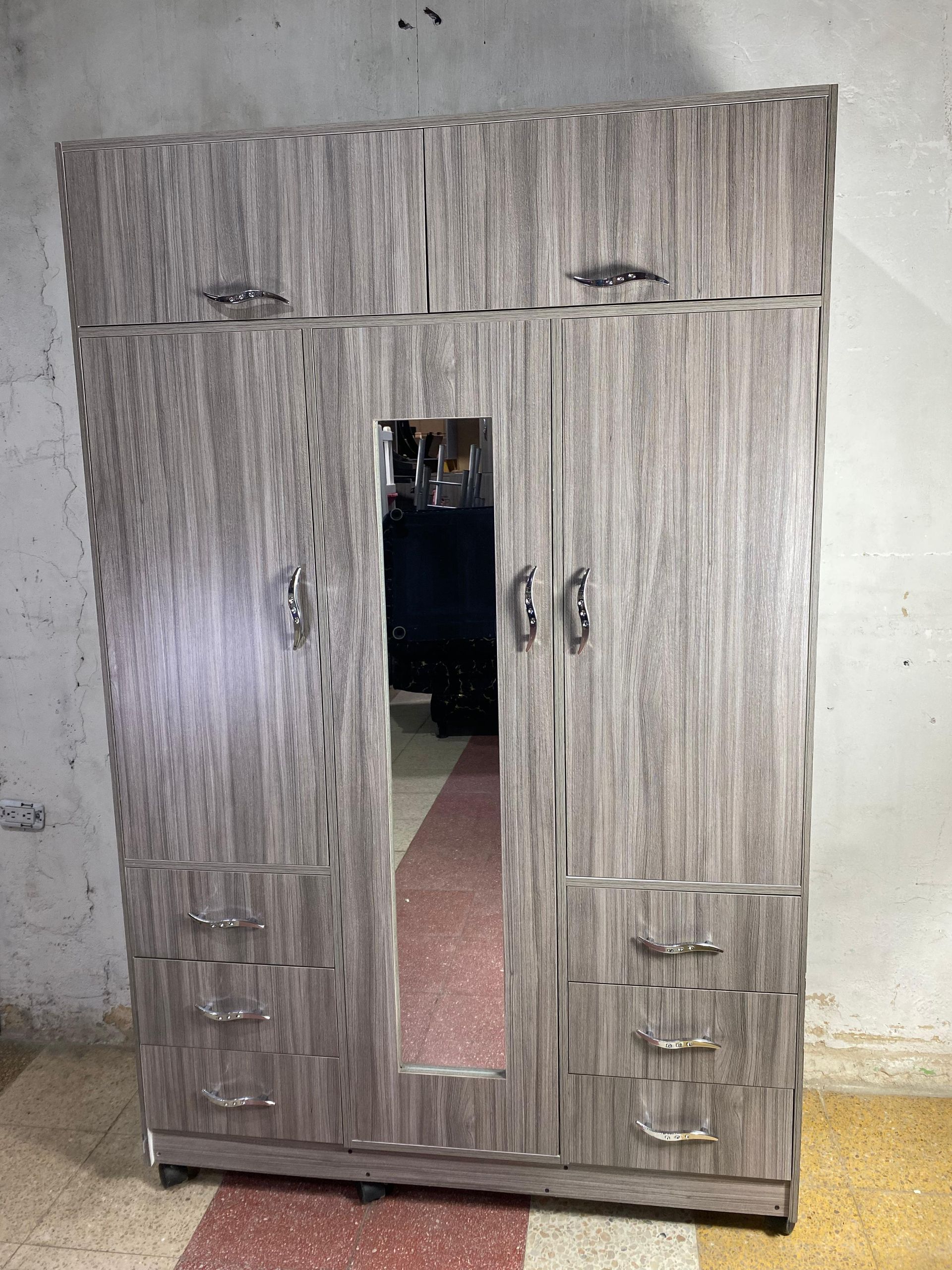 Armario de madera con acabado veta de madera gris, espejo y tiradores plateados.