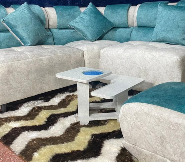 Sofá seccional en forma de L en color blanco y verde azulado con almohadones a juego, mesa de centro blanca y alfombra estampada.