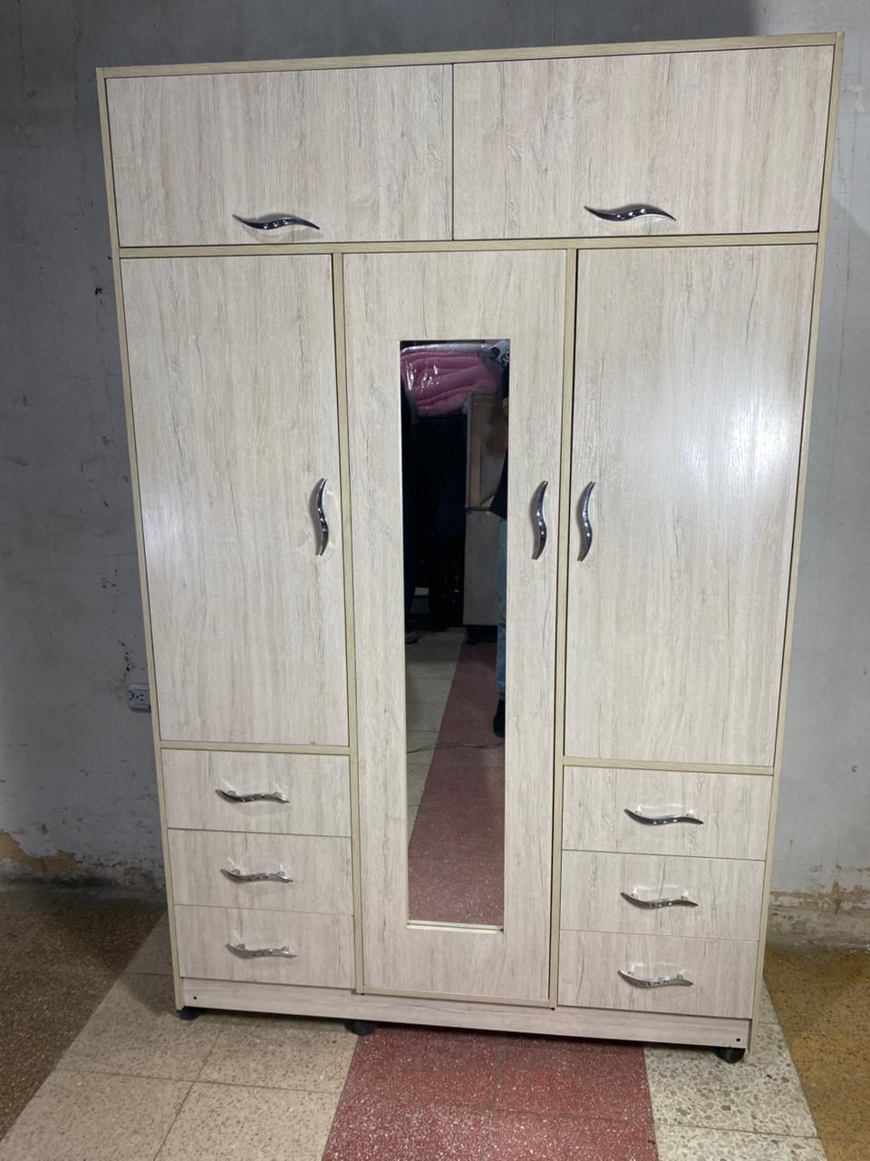 Armario de madera clara con espejo central, cajones y tres puertas superiores.