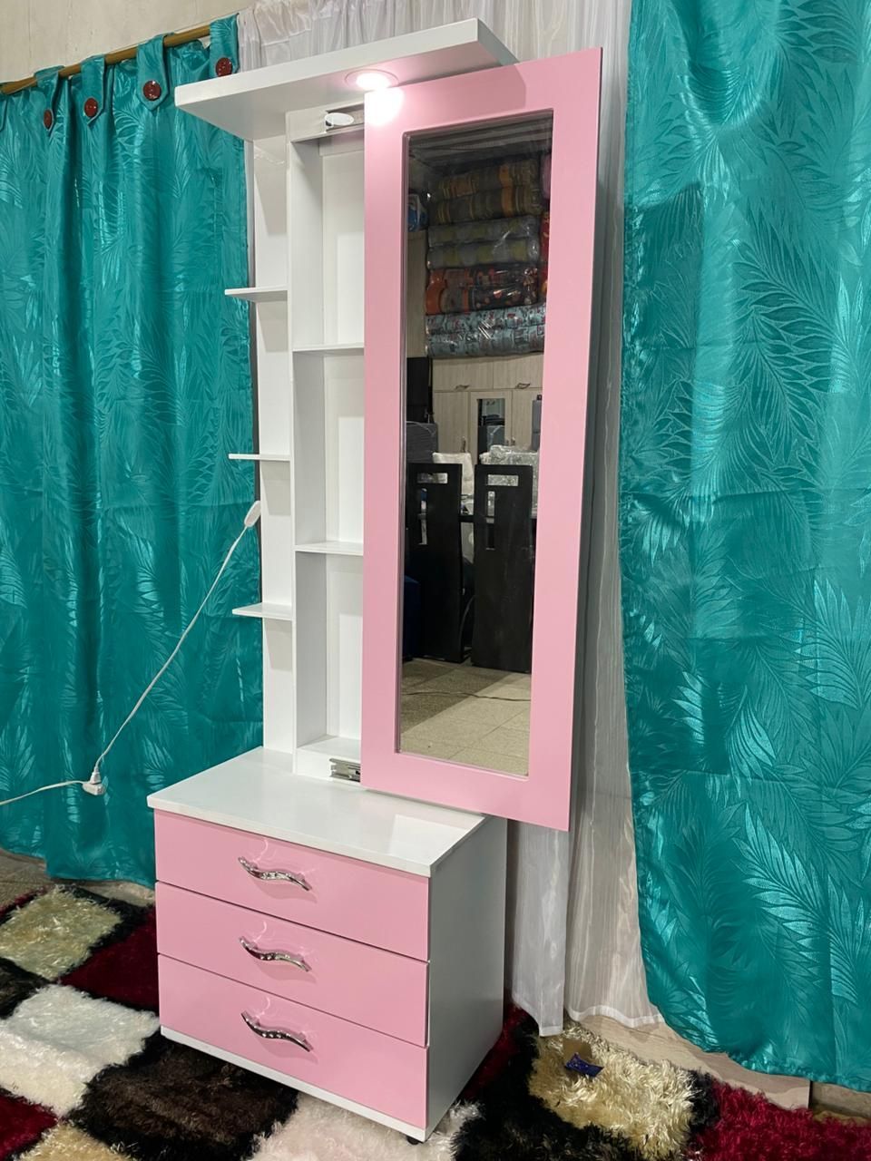 Tocador rosa y blanco con espejo y cajones contra cortinas turquesas.